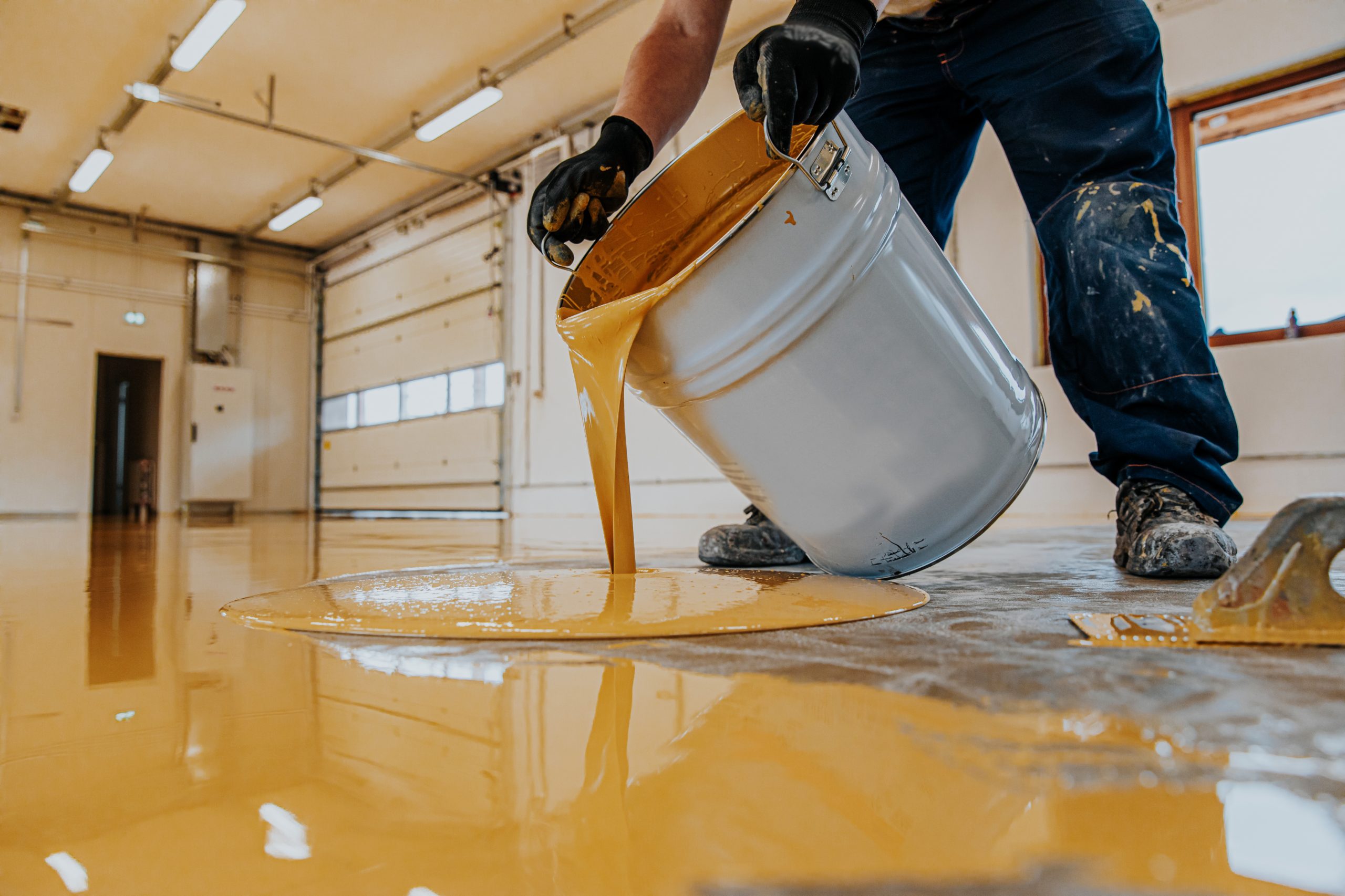 Worker applying a yellow epoxy resin bucket on floor.Construction series